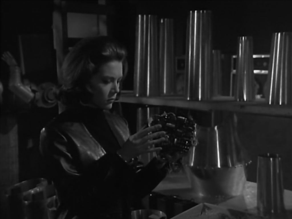 Illustration from the novel theMystery.doc by Matthew McIntosh. Black-and-white shot from TV: a mod young woman wearing a black turtleneck holding a robotic brain.