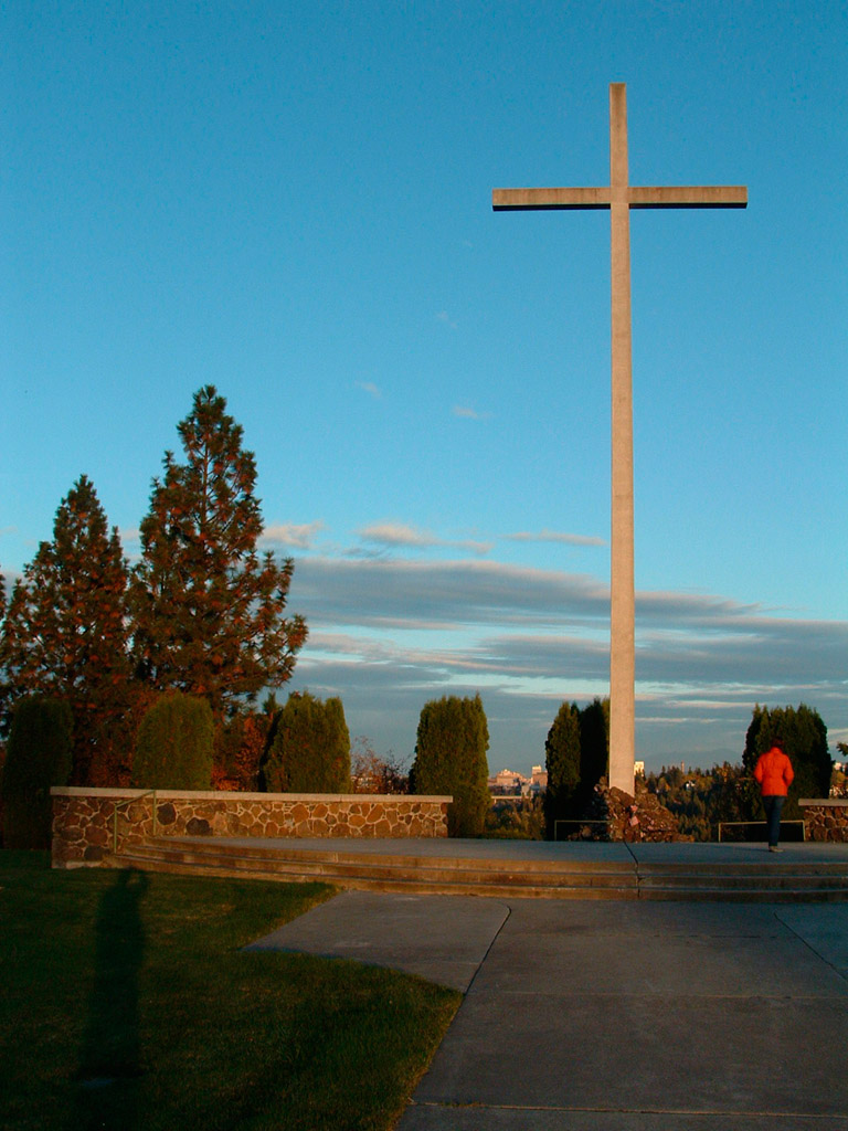 Illustration from the novel theMystery.doc by Matthew McIntosh. Color photo of a woman in a cemetery walking toward a tall 100-foot cross. (c) Matthew McIntosh.